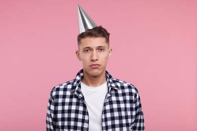 Sad man in party hat on pink background