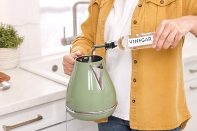 Photo of Woman pouring vinegar from bottle into electric kettle in kitchen, closeup