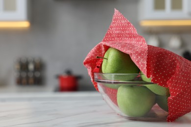 Apples in bowl covered with beeswax food wrap on white table, closeup. Space for text