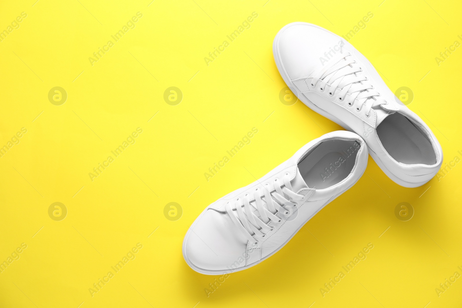 Photo of Pair of stylish white sneakers on yellow background, top view. Space for text