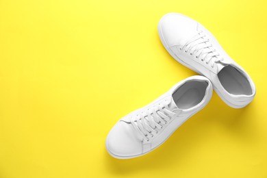 Photo of Pair of stylish white sneakers on yellow background, top view. Space for text