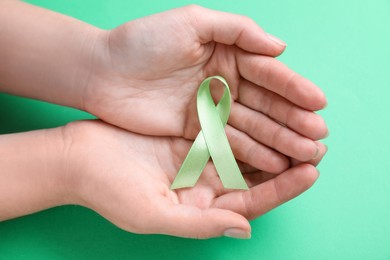 World Mental Health Day. Woman holding green ribbon on color background, top view