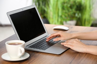 Photo of Woman working with laptop at wooden table, closeup