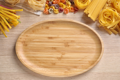 Photo of Flat lay composition with different types of pasta and empty plate on wooden background. Space for text