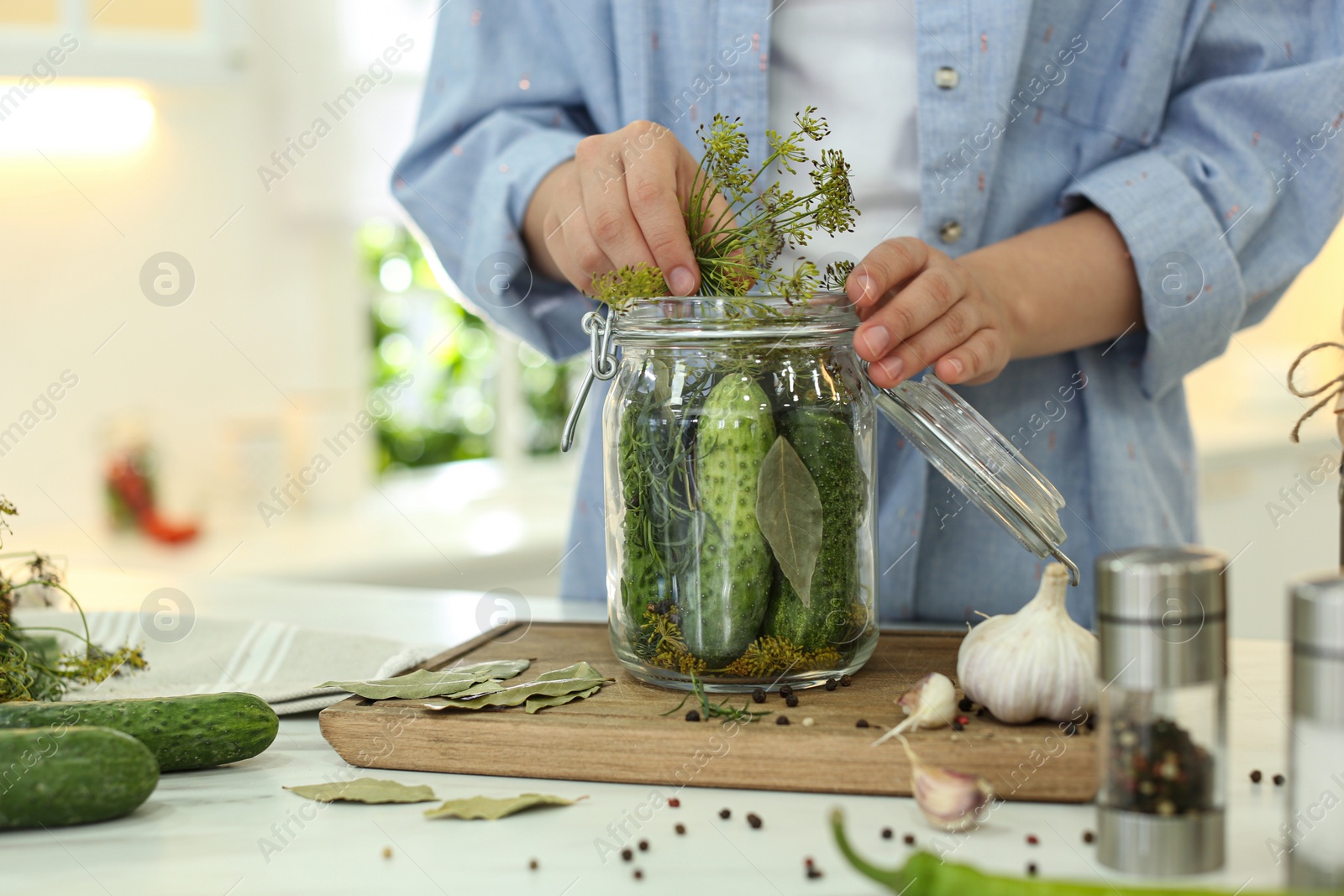 Photo of Woman putting dill into pickling jar at table in kitchen, closeup