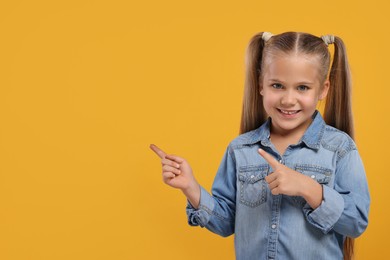 Photo of Special promotion. Little girl pointing at something on orange background. Space for text