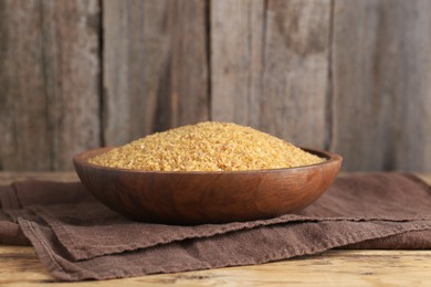 Bowl with uncooked bulgur and napkin on wooden table