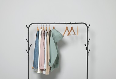 Photo of Rack with stylish clothes on wooden hangers against light grey background