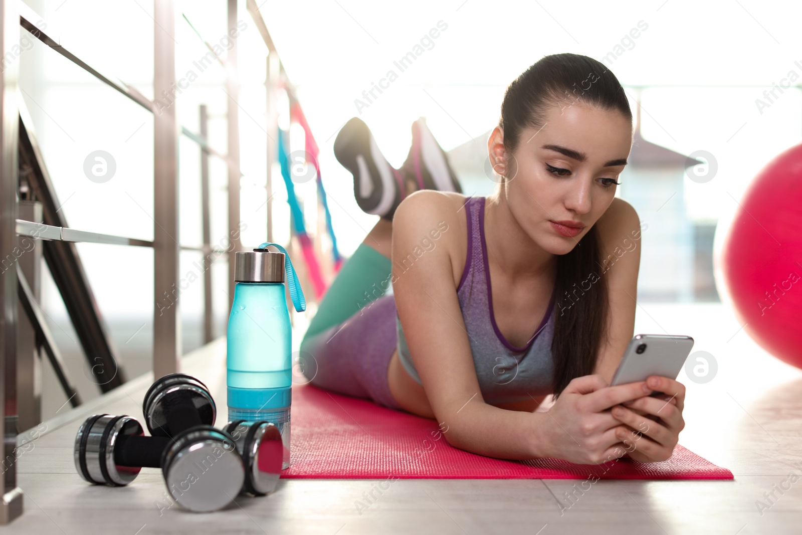 Photo of Lazy young woman with smartphone on yoga mat indoors