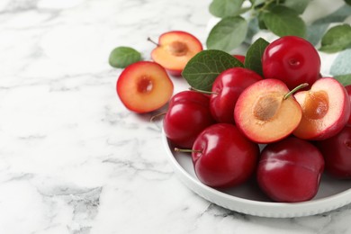 Photo of Delicious ripe cherry plums with leaves on white marble table. Space for text