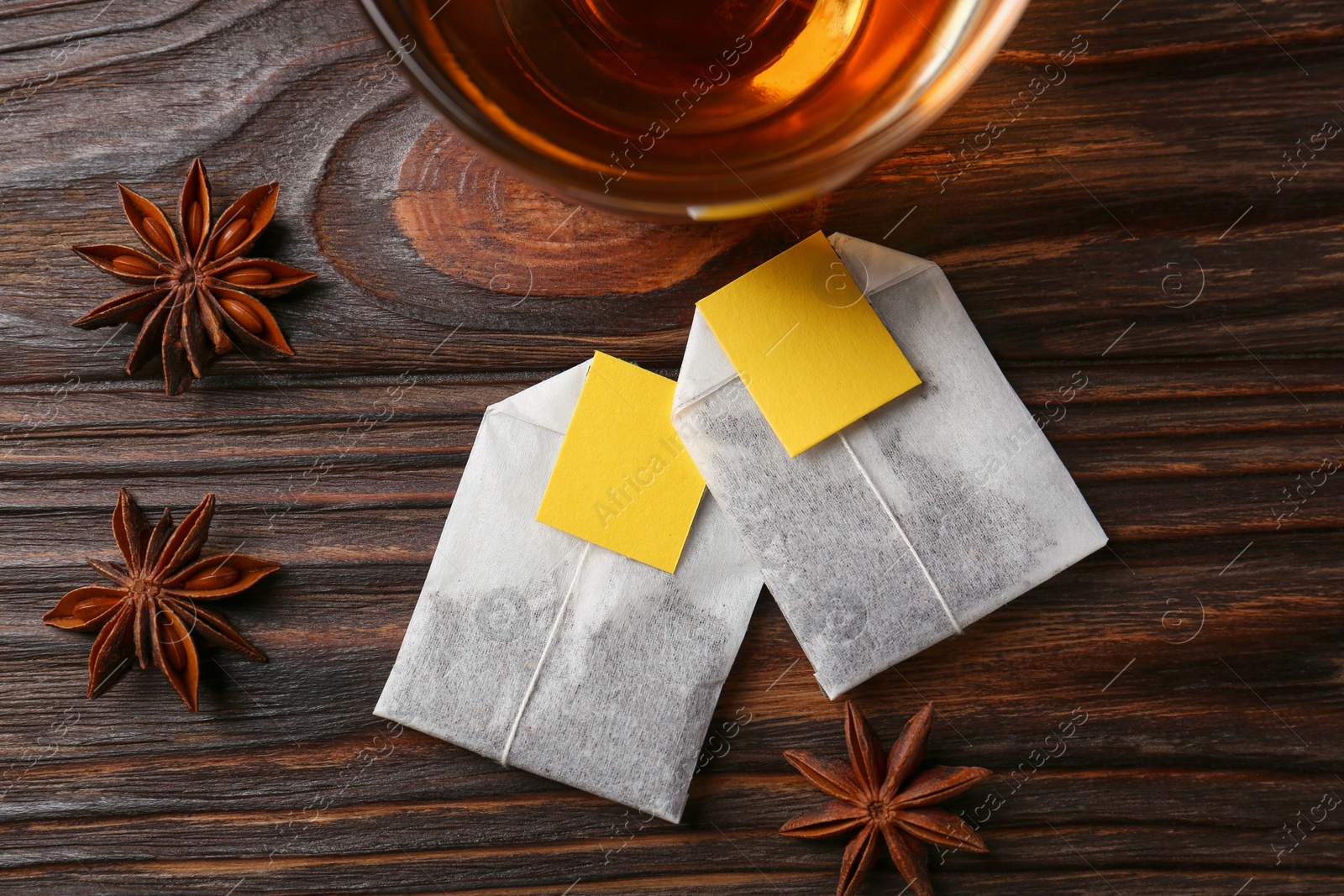 Photo of Tea bags, cup of hot drink and anise stars on wooden table, flat lay