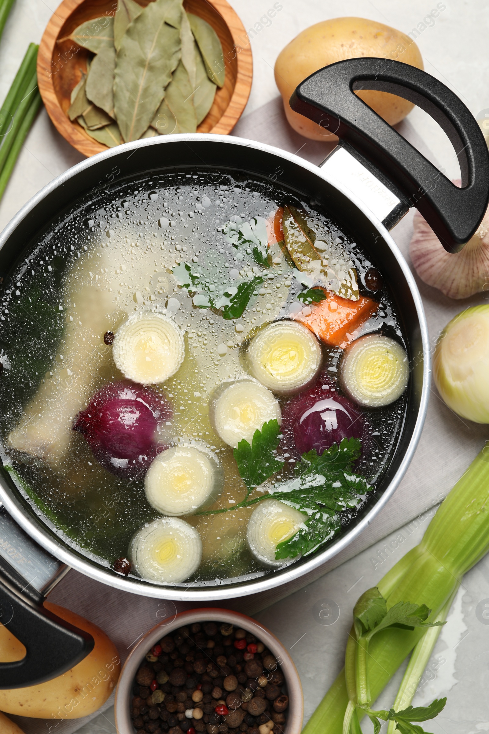 Photo of Pot with tasty bouillon and different ingredients on light grey table, flat lay