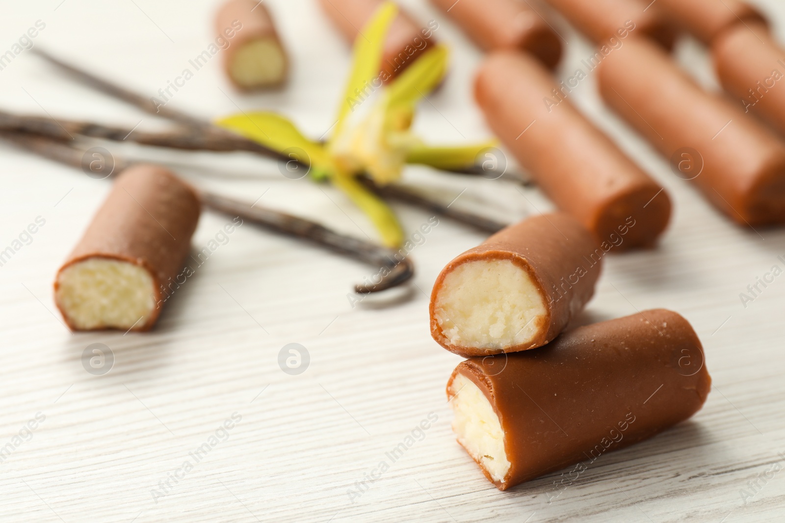 Photo of Glazed curd cheese bars, vanilla pods and flower on white wooden table, closeup