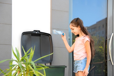 Photo of Girl throwing plastic bottle into recycling bin outdoors