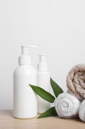 Bottles of cosmetic products, leaves and towels on wooden table