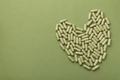 Photo of Heart made of vitamin capsules on olive background, top view. Space for text