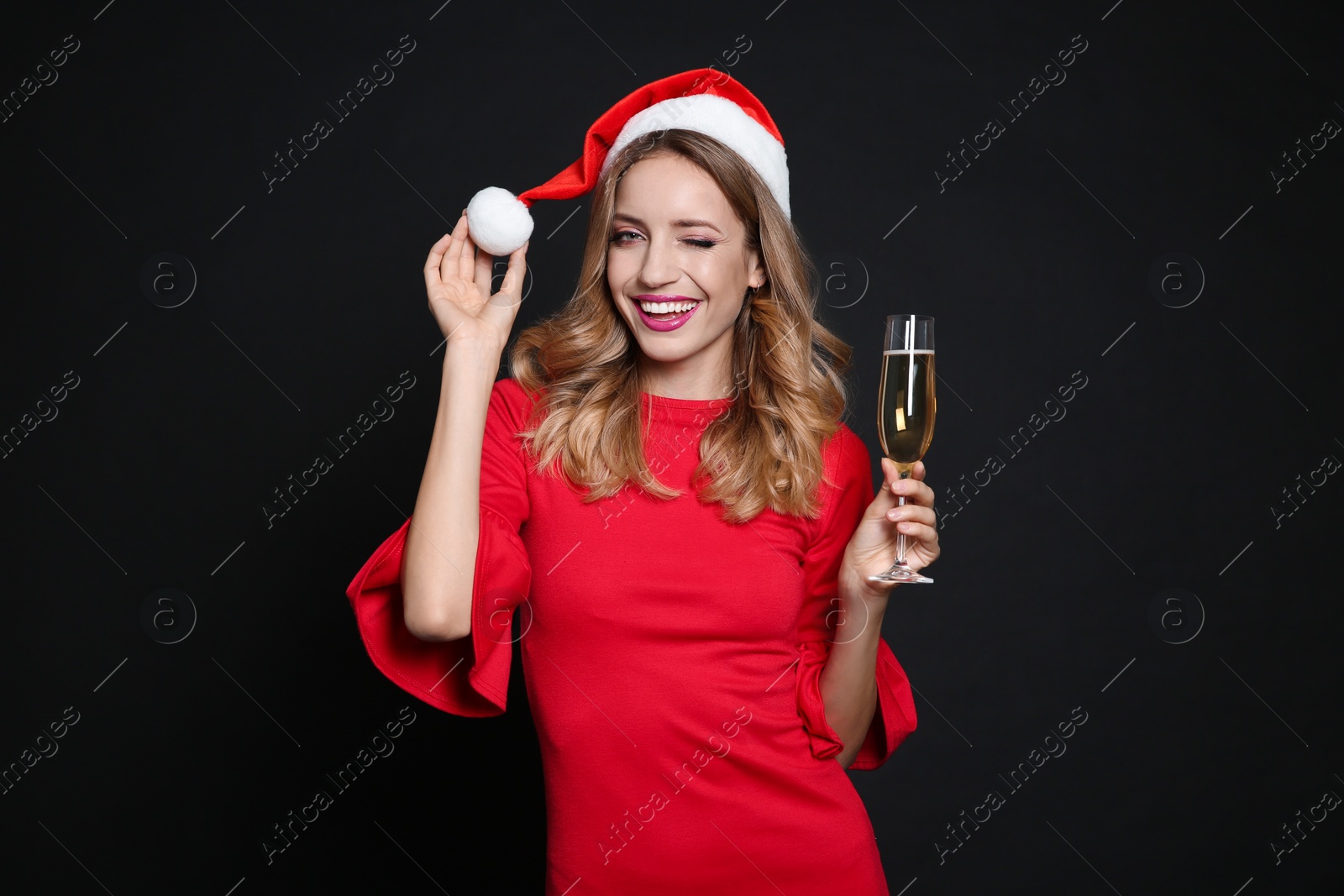 Photo of Happy woman in Santa hat with glass of champagne on black background. Christmas party