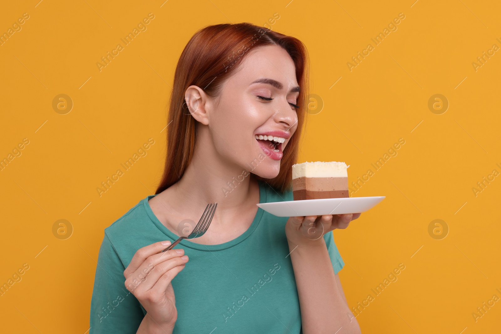 Photo of Young woman eating piece of tasty cake on orange background