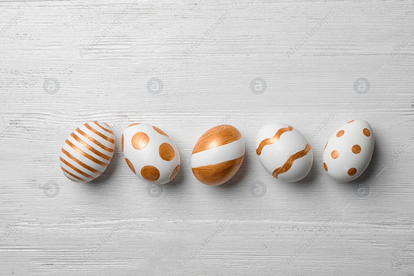 Photo of Set of traditional Easter eggs decorated with golden paint on wooden background, top view