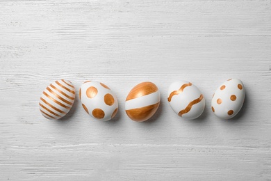 Photo of Set of traditional Easter eggs decorated with golden paint on wooden background, top view