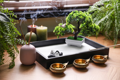 Photo of Beautiful miniature zen garden, incense sticks and oil lamps near window indoors