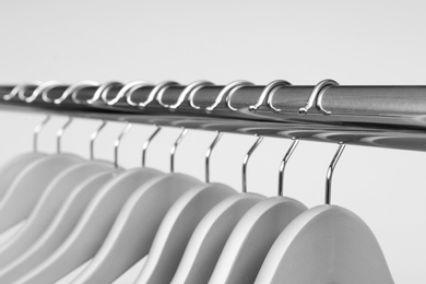 Photo of Empty clothes hangers on metal rail against light background, closeup