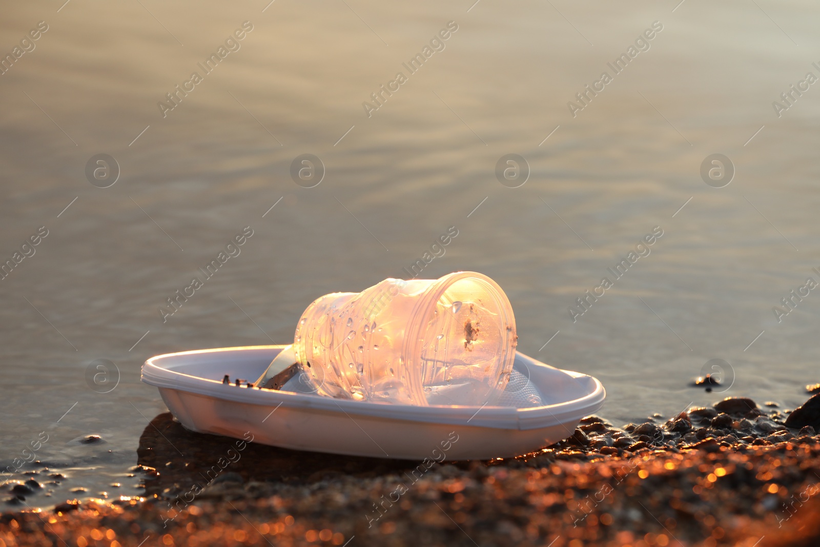 Photo of Used plastic tableware in water outdoors, space for text. Environmental pollution concept