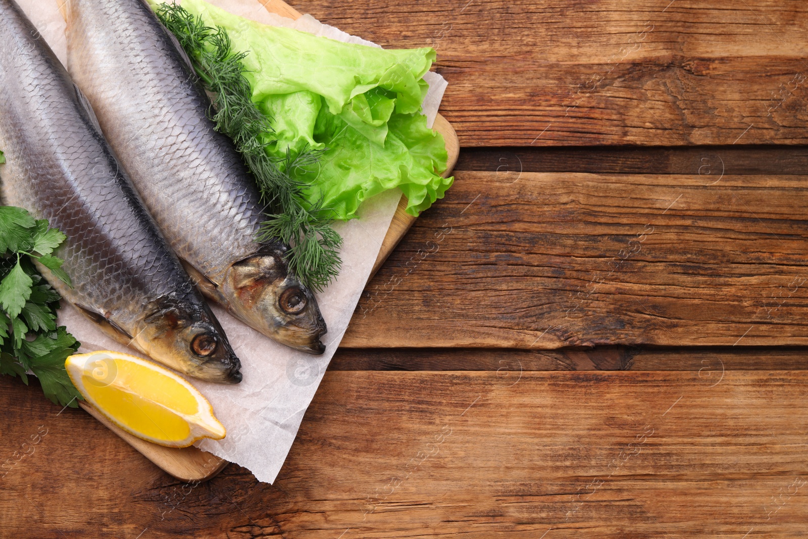 Photo of Board with delicious salted herrings, lemon and herbs on wooden table, top view. Space for text