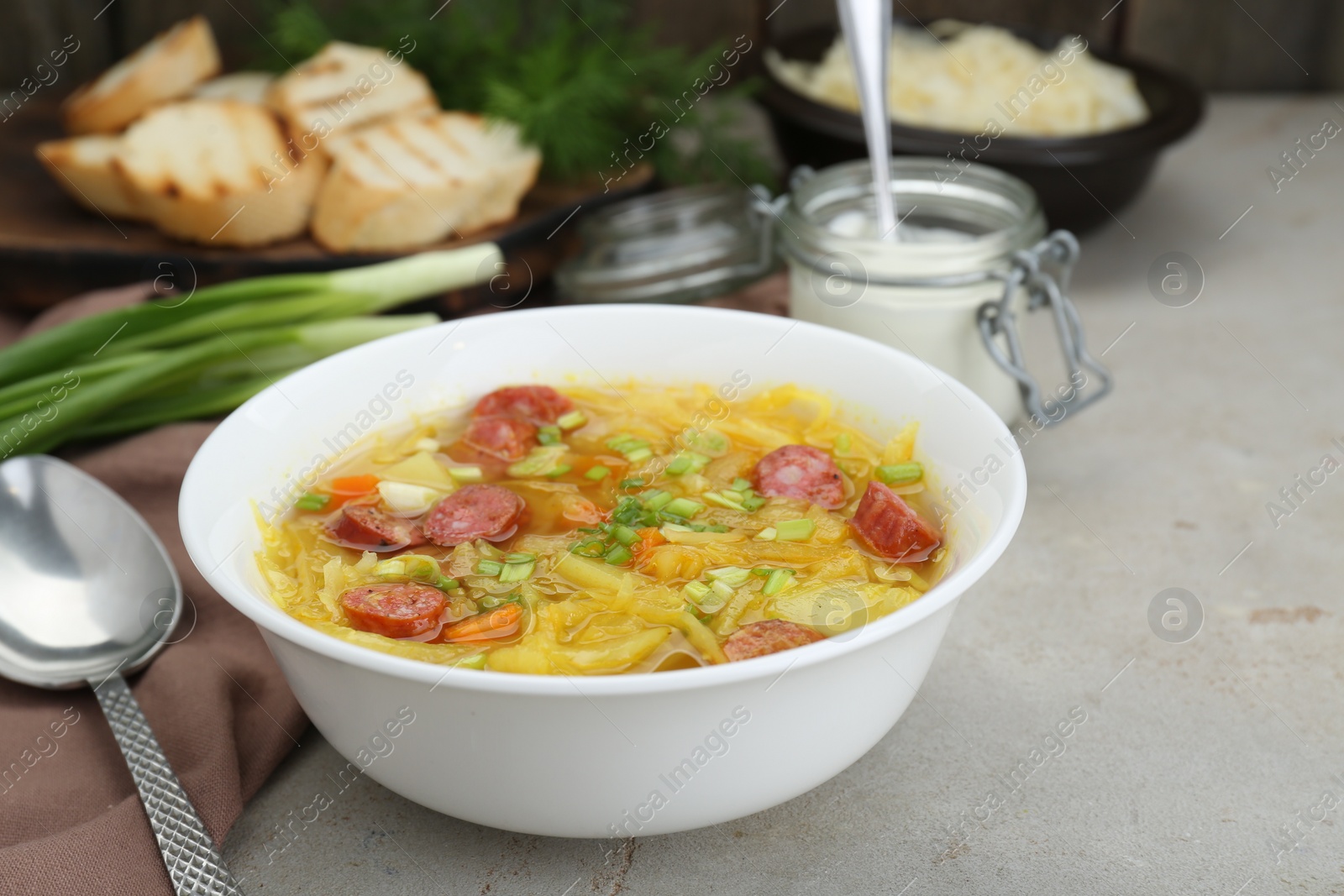 Photo of Delicious sauerkraut soup with smoked sausages and green onion served on light grey table