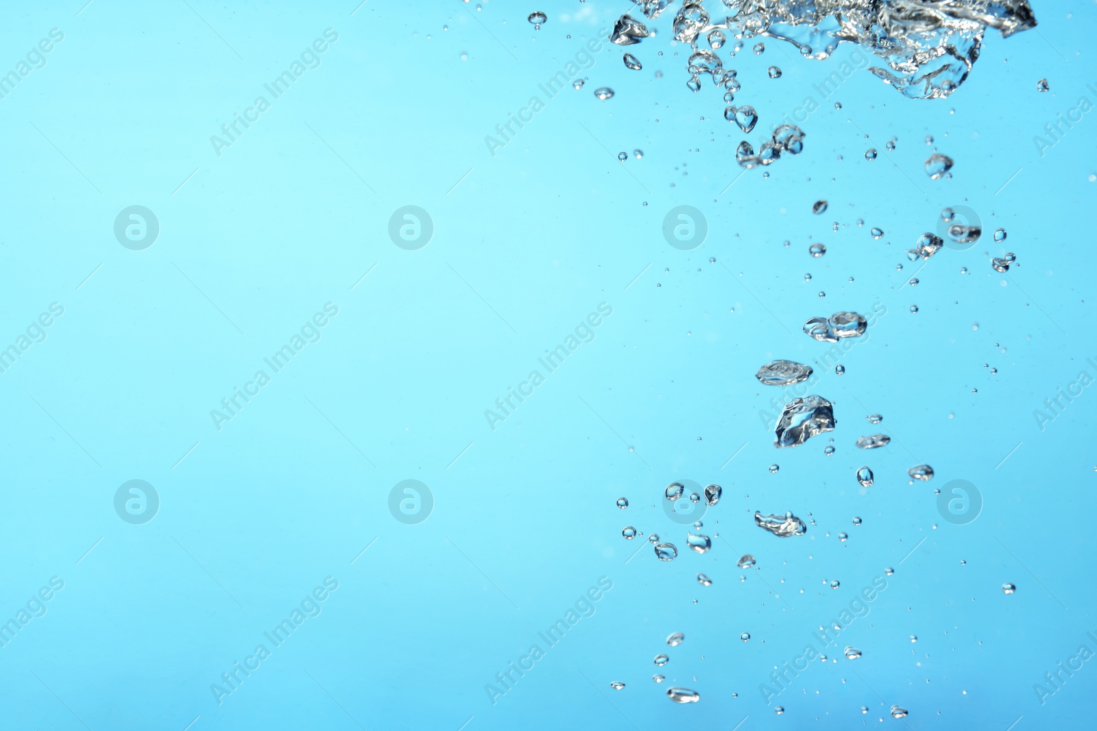 Photo of Air bubbles in water on light blue background. Space for text