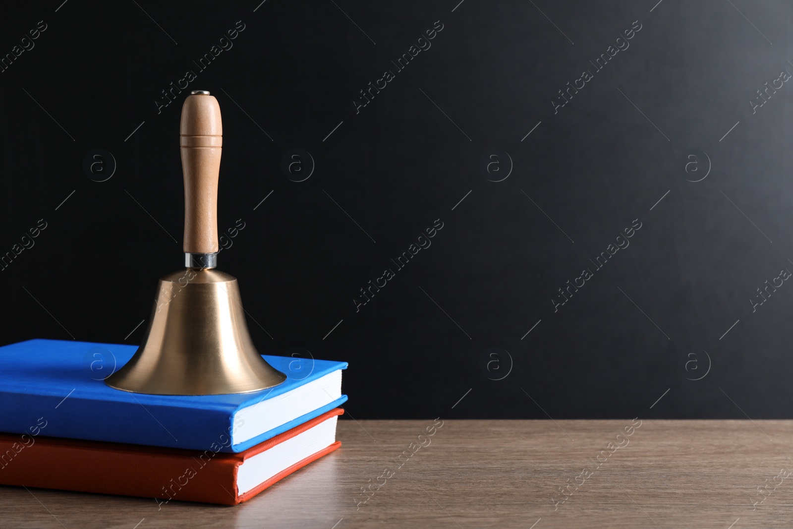 Photo of Golden bell and books on wooden table near blackboard, space for text. School days