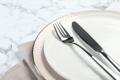 Clean plates, cutlery and napkin on white marble table, closeup