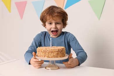 Photo of Cute boy with birthday cake at white table indoors