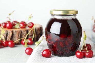 Photo of Jar of pickled cherries and fresh fruits on light table, closeup