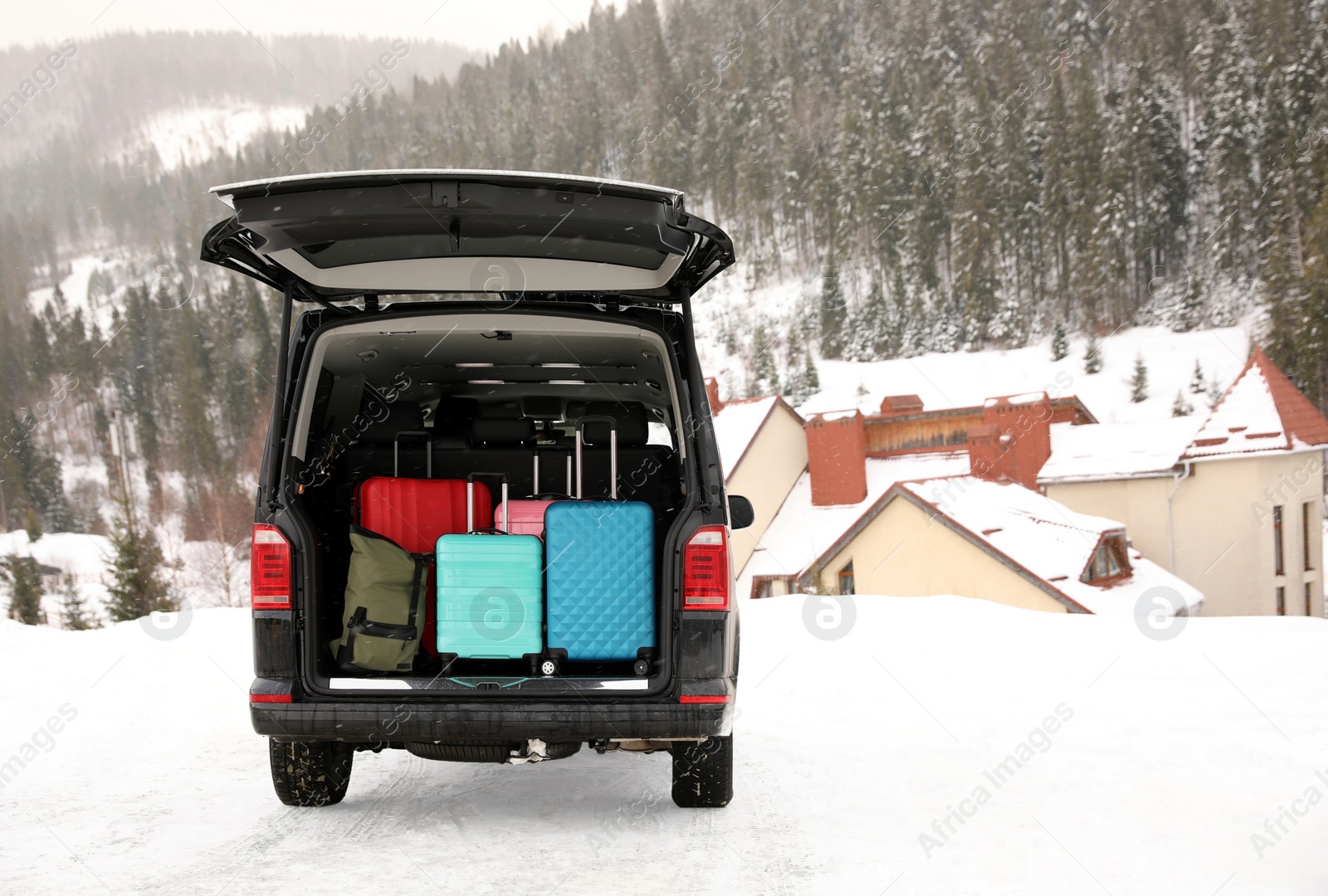 Photo of Black car with luggage in trunk on snowy road. Winter vacation