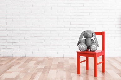 Stuffed toy rabbit on chair in child room. Space for text