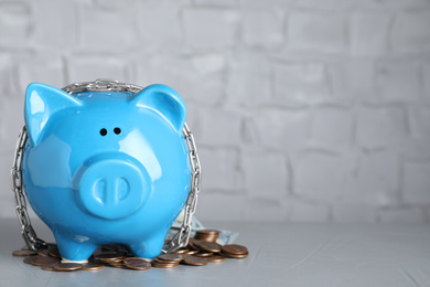 Photo of Piggy bank with steel chain and coins on grey stone table, space for text. Money safety concept