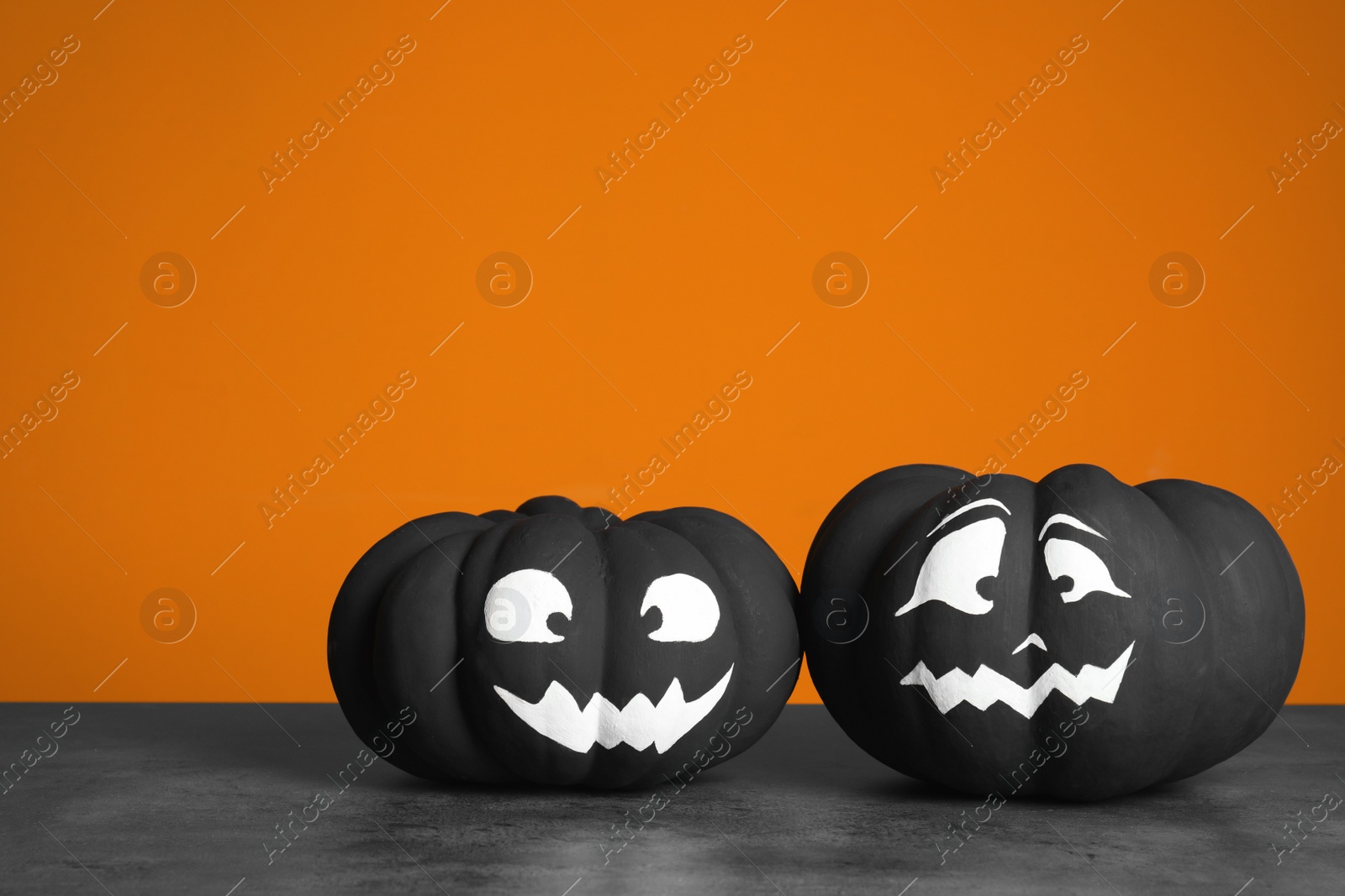 Photo of Pumpkins with scary faces on table against color background, space for text. Halloween decor