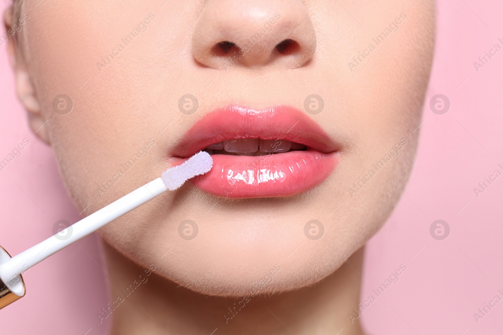 Photo of Beautiful young woman applying gloss on her perfect lips, closeup