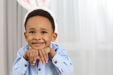 Photo of Cute African American boy with Easter bunny ears headband indoors, space for text