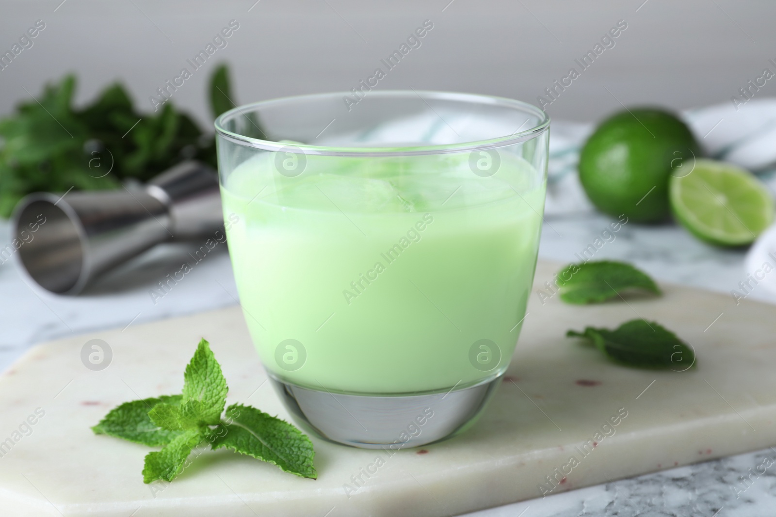 Photo of Delicious mint liqueur with ice cubes and green leaves on white marble table, closeup