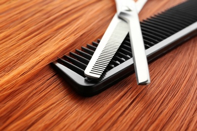 Photo of Thinning scissors and comb on red hair, closeup. Hairdresser service