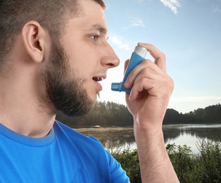 Image of Man using asthma inhaler near lake. Emergency first aid during outdoor recreation