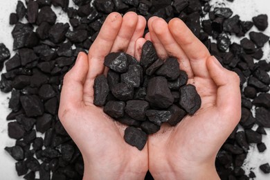 Woman with handful of coal over pile on white background, top view