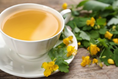 Photo of Cup of aromatic celandine tea and flowers on wooden table, closeup. Space for text