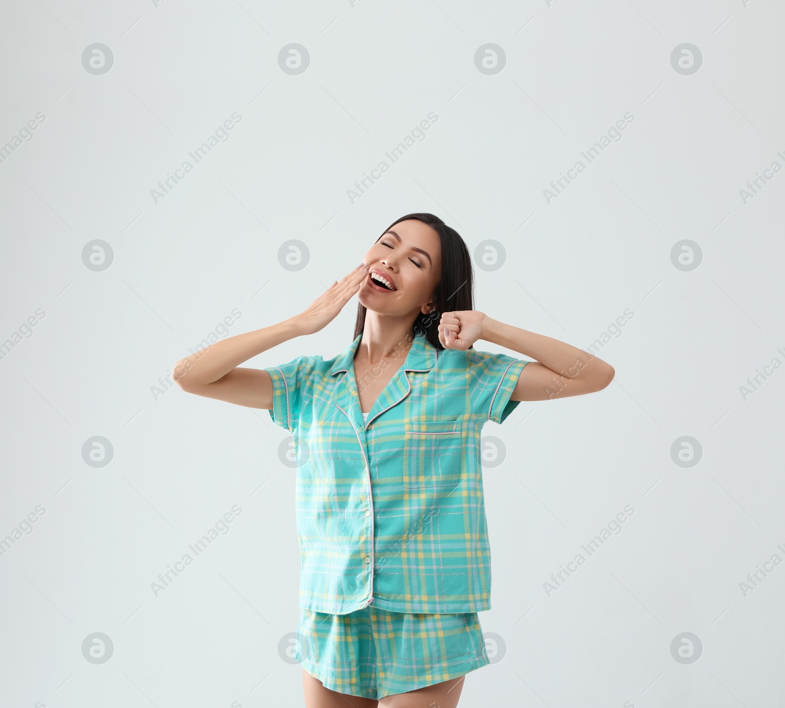 Photo of Beautiful Asian woman in pajamas yawning on light grey background. Bedtime