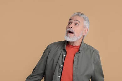 Portrait of surprised senior man on beige background, space for text