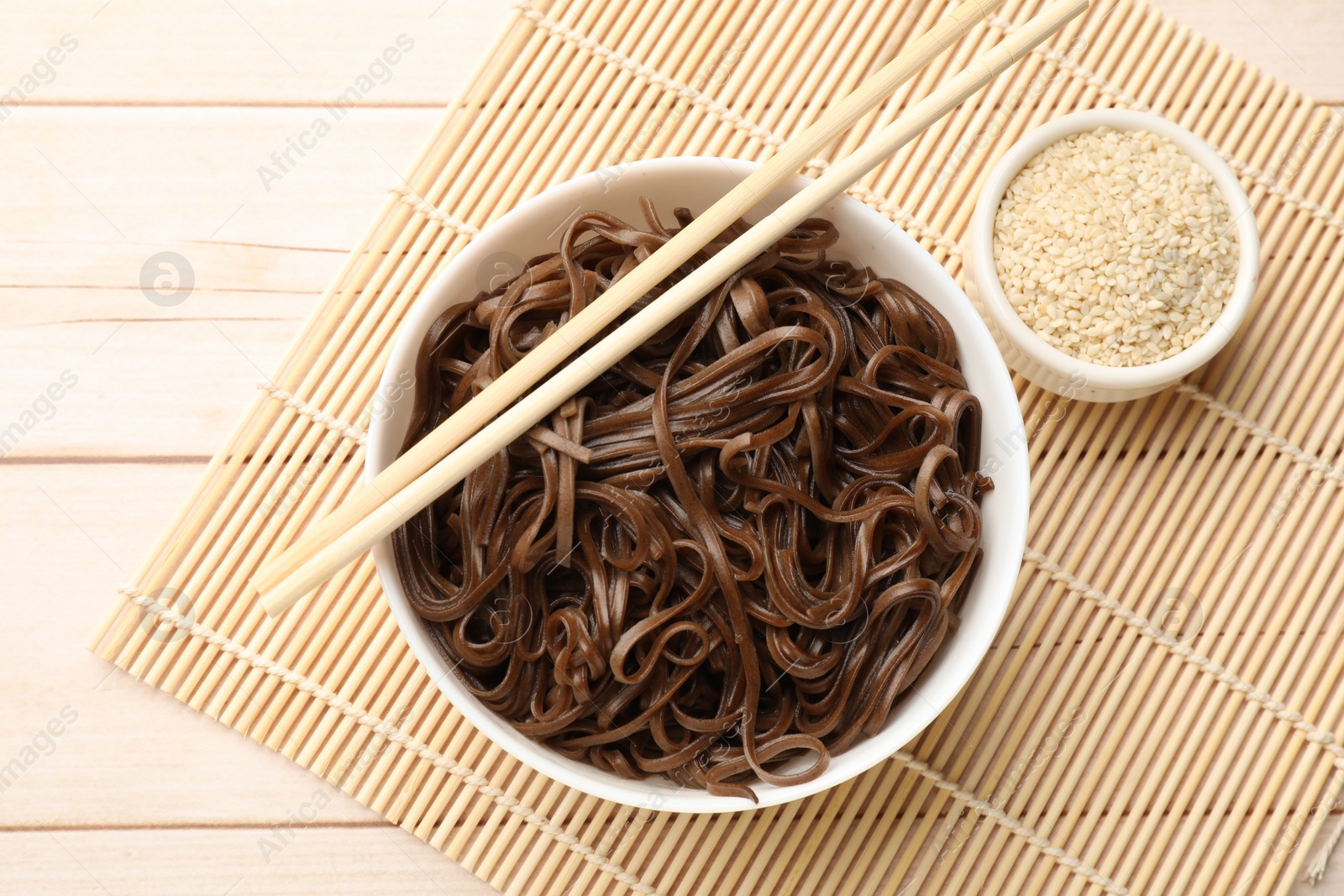 Photo of Tasty buckwheat noodles (soba) with sesame and chopsticks on wooden table, flat lay