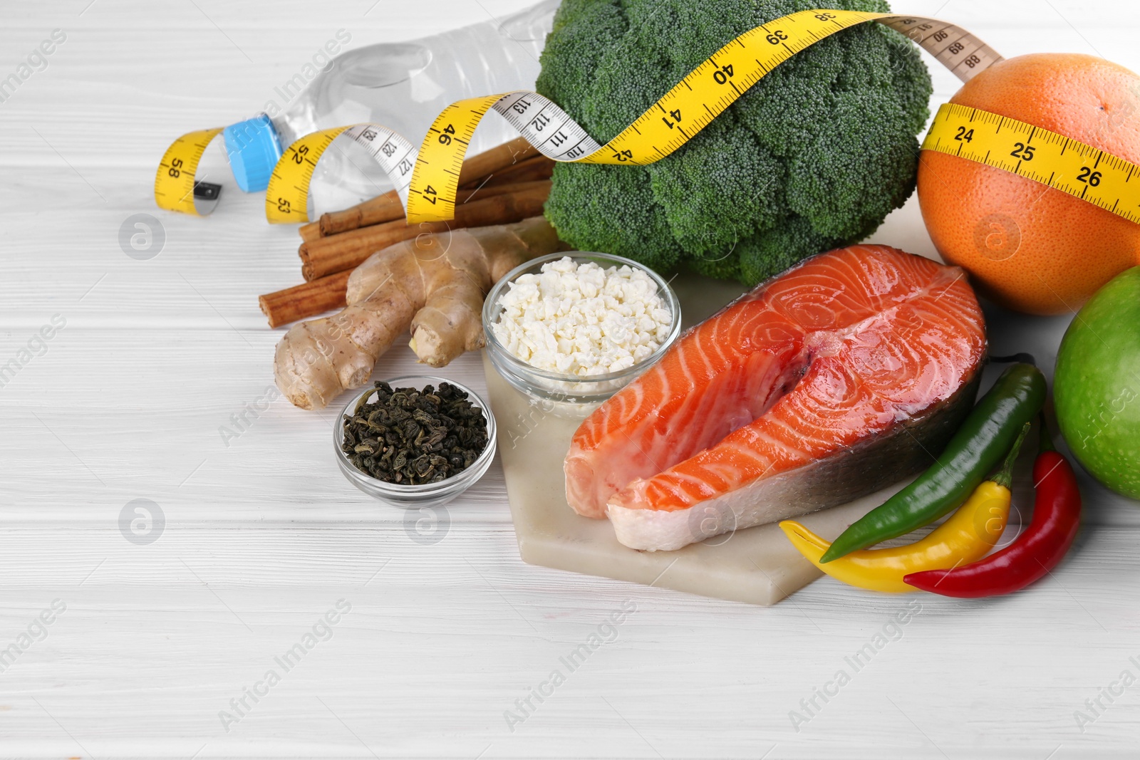 Photo of Metabolism. Different food products and measuring tape on white wooden table