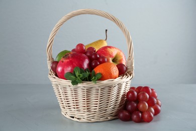 Wicker basket with different ripe fruits on grey table